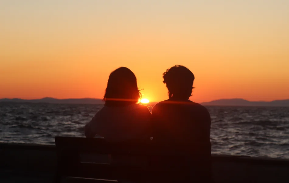 Two people sitting on a bench watching the sunset.