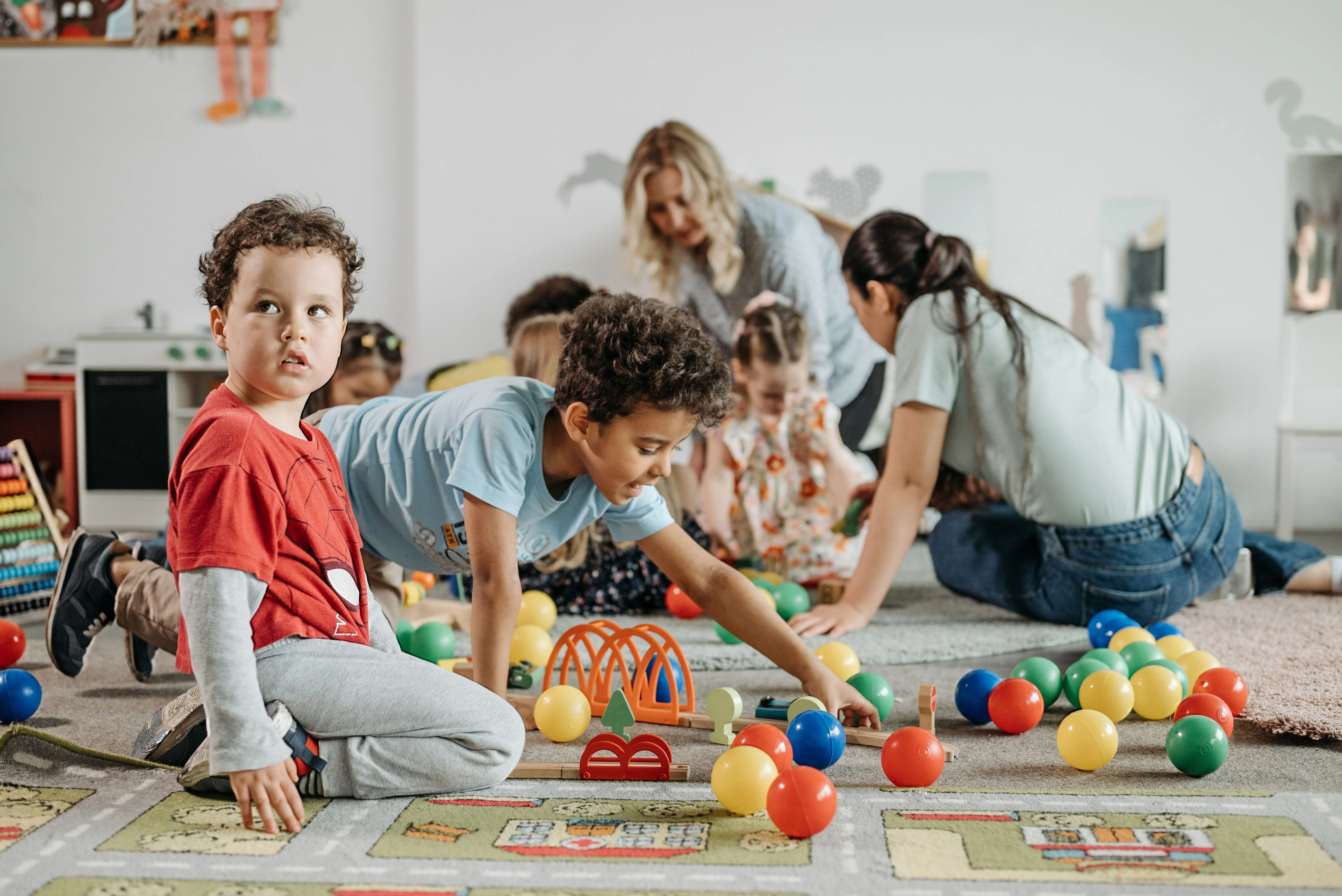 Children and adults playing with colorful toys on a classroom floor.